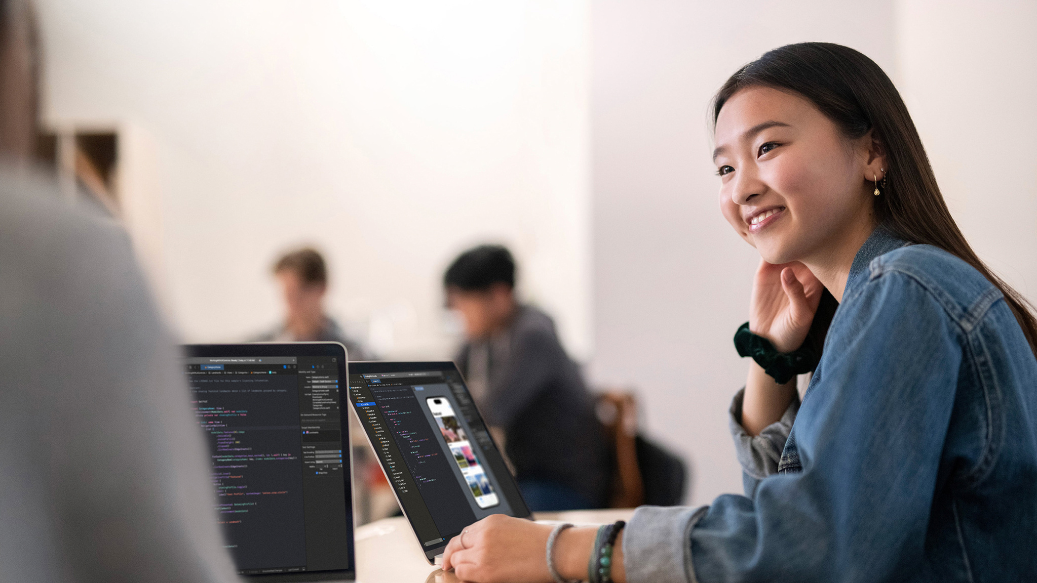 An image of a developer in a classroom-type setting who’s smiling as she sits in front of a MacBook.