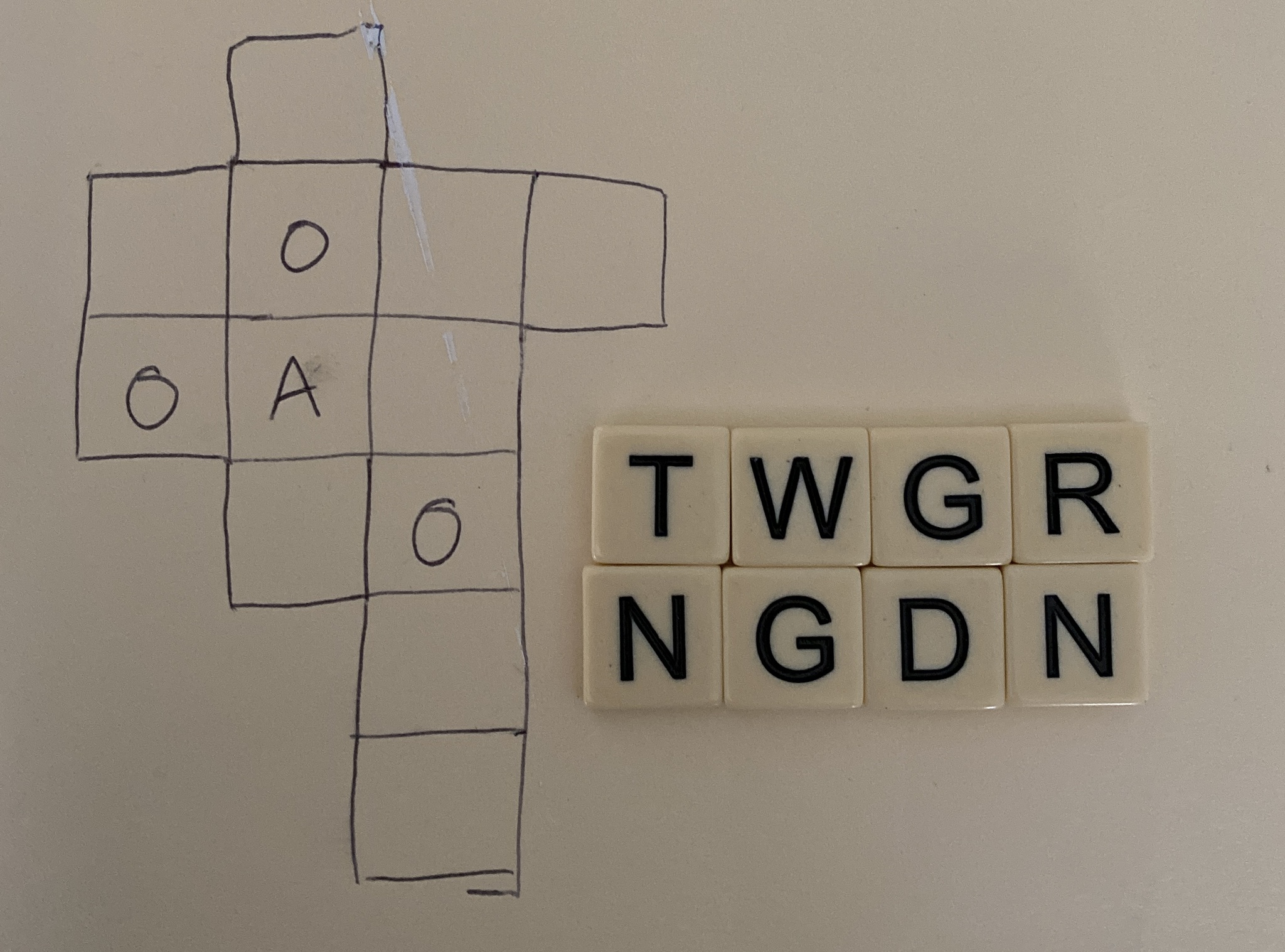 An early Knotwords prototype experiment: A handwritten Knotwords puzzle containing just a few letters sits next to eight physical titles with one letter each.