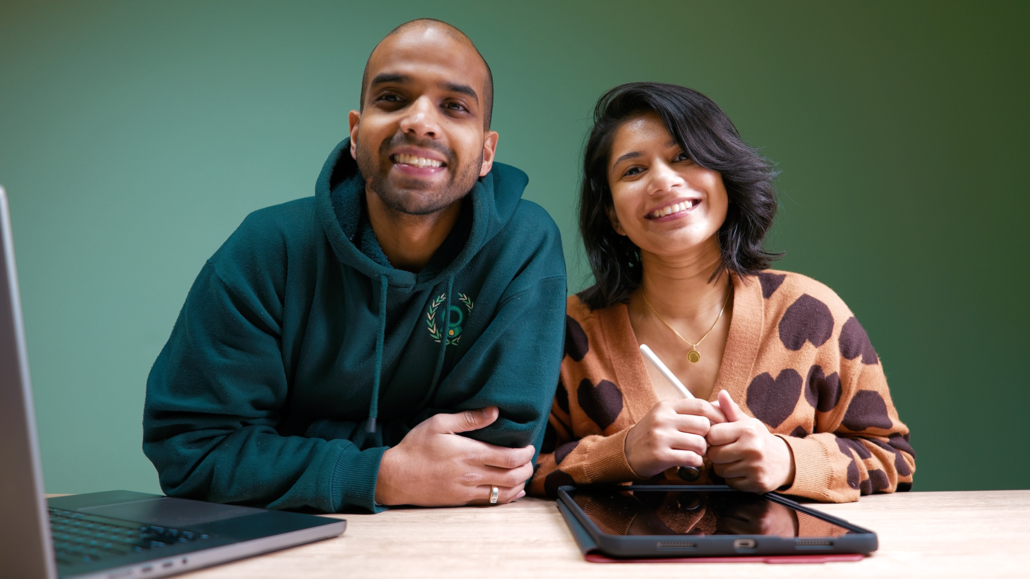 A photo of the Australian husband-and-wife team who developed Bears Gratitude, Isuru Wanasinghe and Nayomi Hettiarachchi, sitting at a table in front of a MacBook and iPad. 