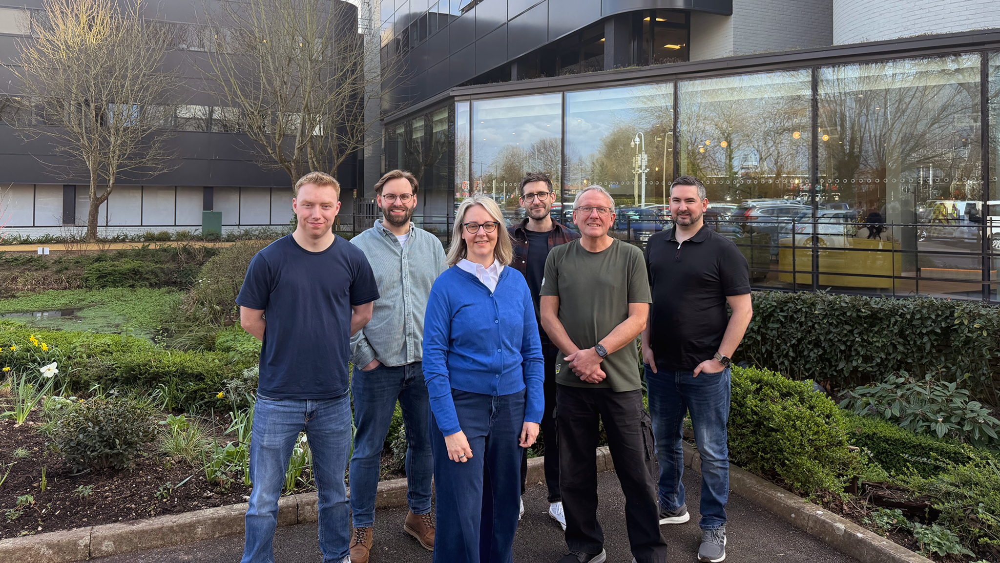 A photograph  of six members of the Plane Finder team, each  lasting  extracurricular  successful  a courtyard adjacent  to an bureau   building.