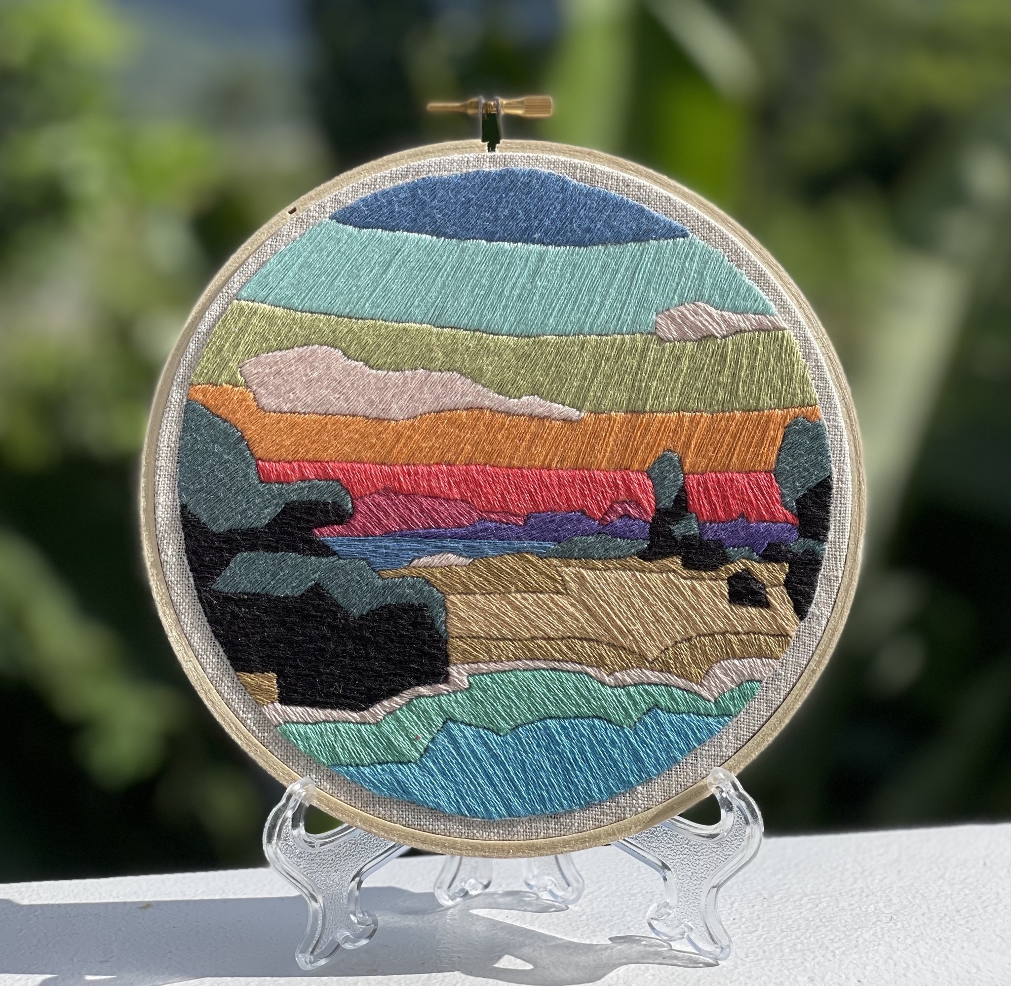 A photo of an embroidery hoop filled with sections of varying colors, including blue, green, orange, and pink. 