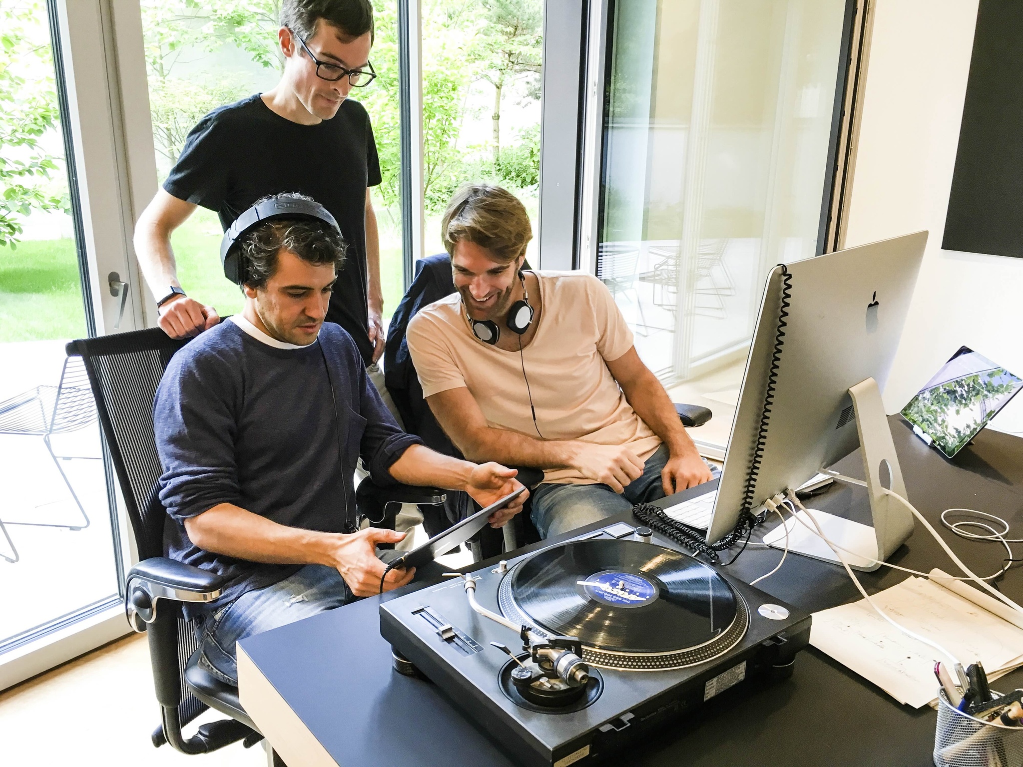 A photo of Karim Morsy and two members of the djay development team, seated in a well-lit office in front of a large iMac screen and turntable deck. 