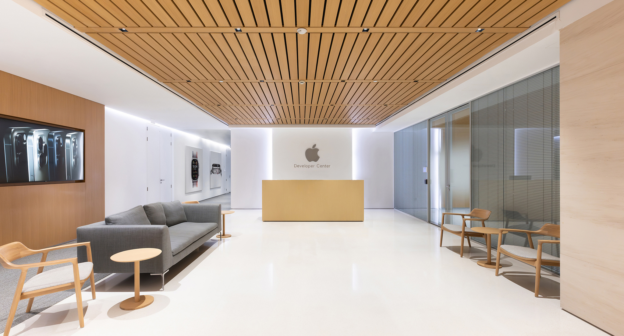 The interior of the Apple Developer Center, an open and brightly lit room with gray sofas, lots of wooden chairs and a reception desk under a large Apple logo.