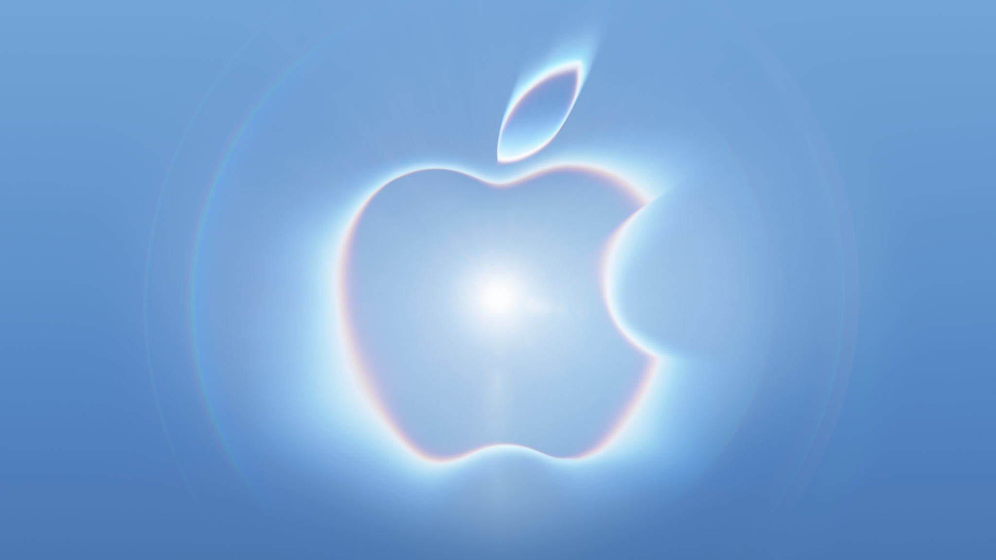 Apple logo glowing with a central lens flare and iridescent, rainbow-refracted edges against a light blue background.